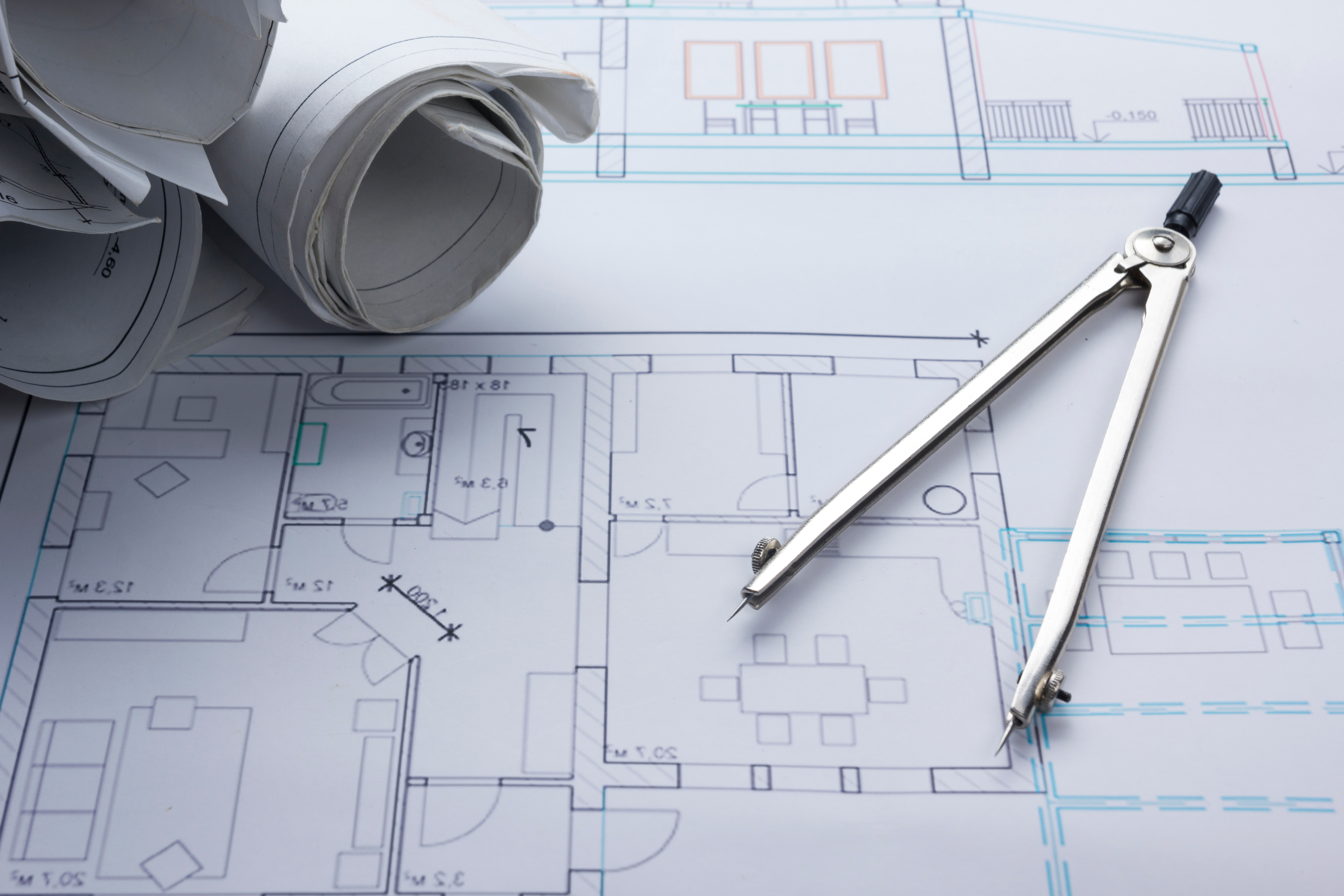Photo of an architect's workspace with a divider compass and rolled blueprints resting on a floor plan.