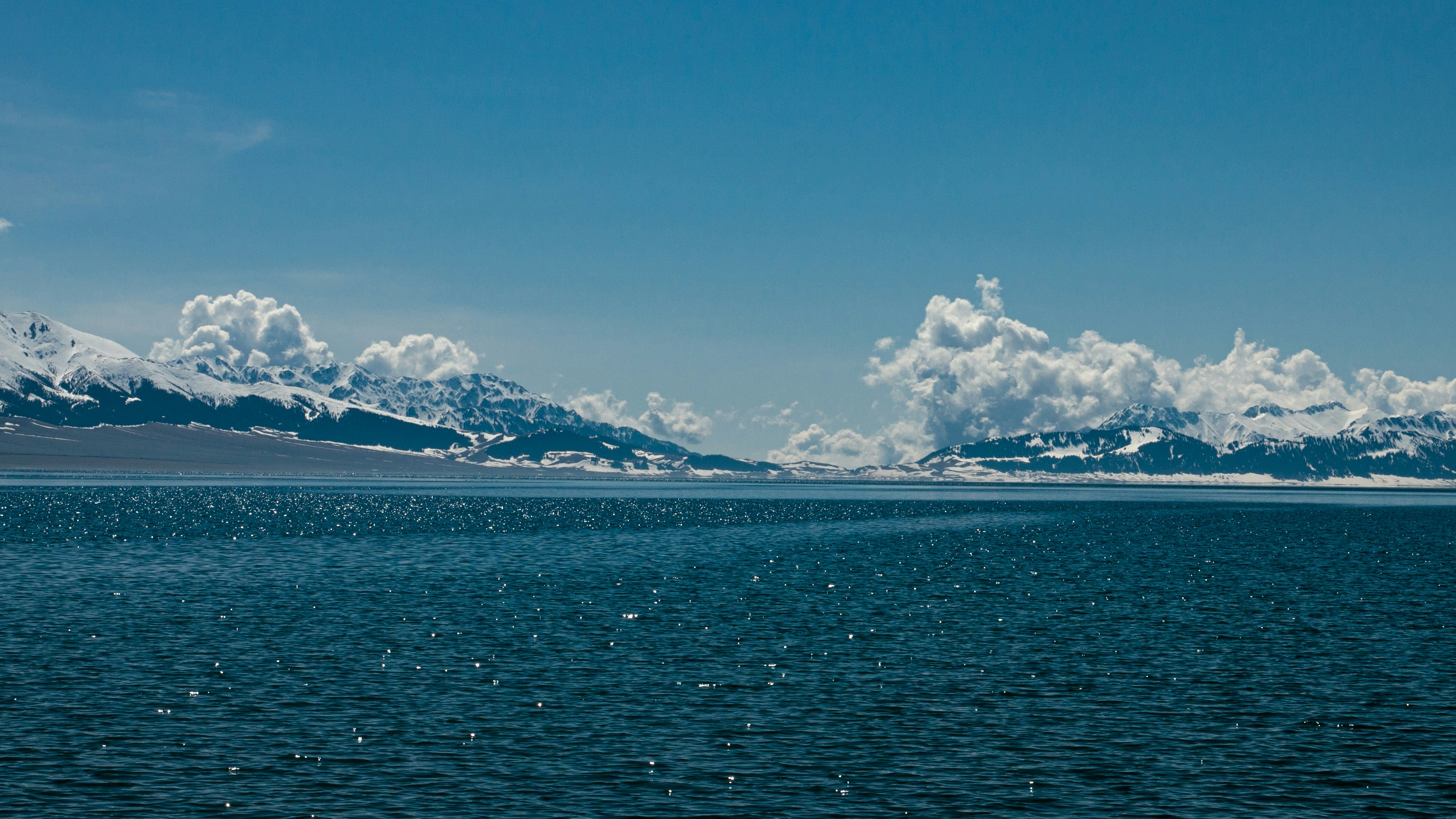 Snowy mountains rise over a blue sea.