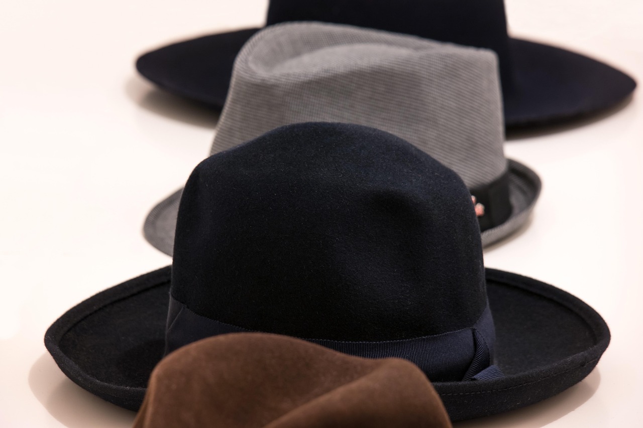 Four hats. From front to back: the crown of a brown fedora, a black fedora with the brim turned up, a grey trilby, and a black fedora with the brim flat
