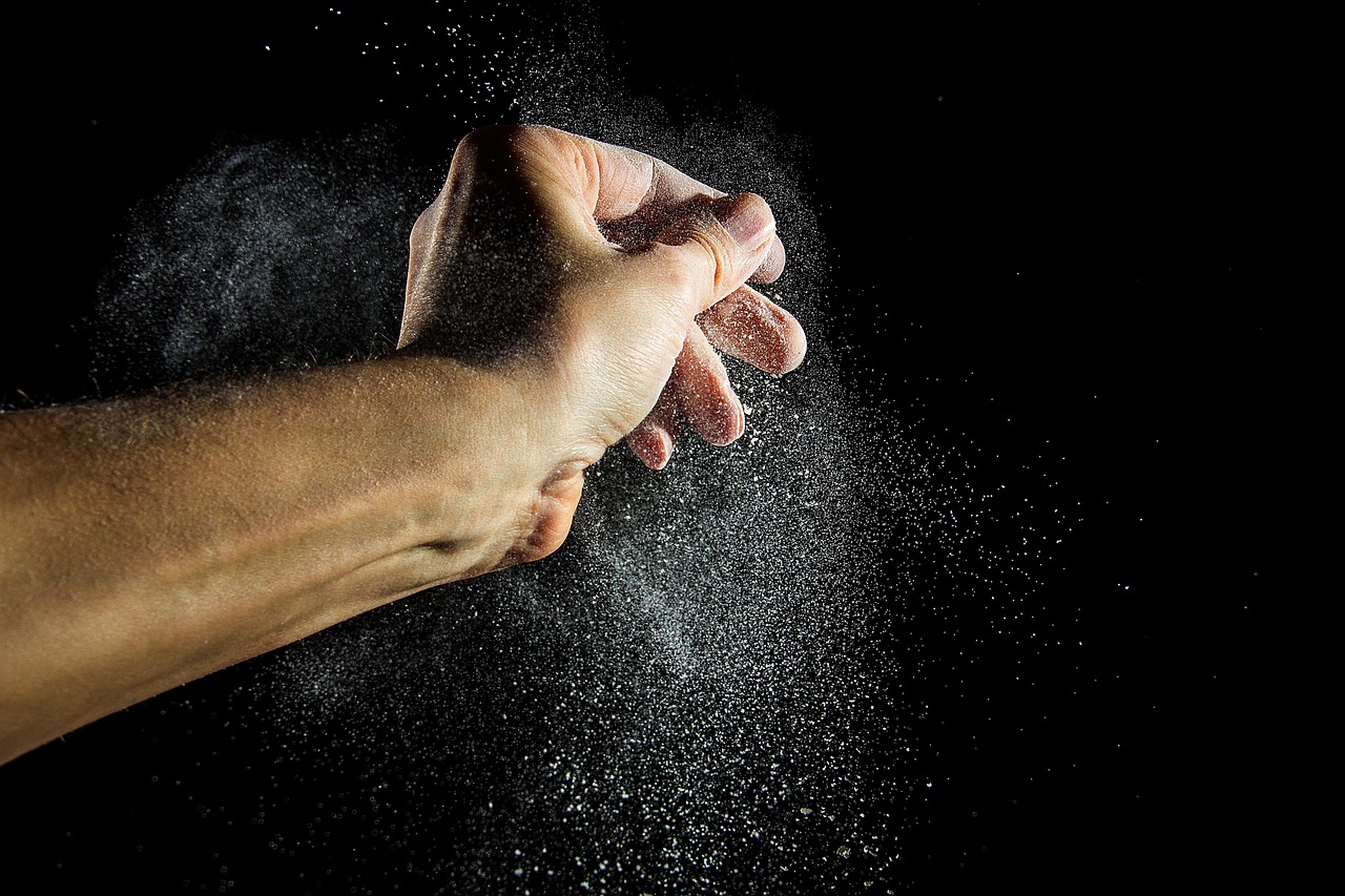 A man's hand scattering flour against a dark background