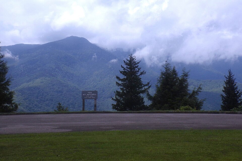 A view of a beautiful blue mountain, Mt. Mitchell, from a highway, with a designating sign of the viewpoint in sight