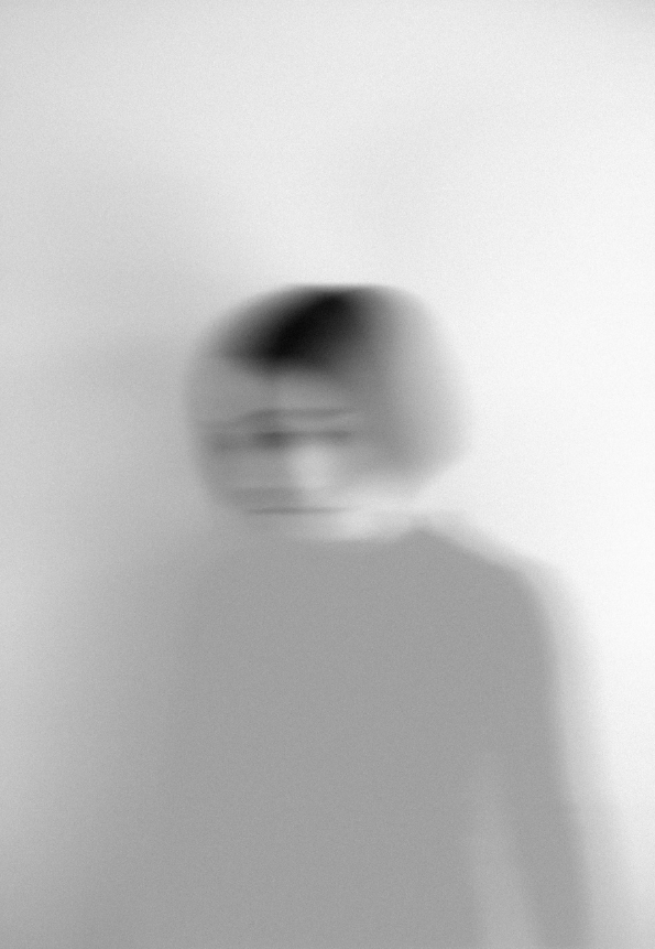A woman with a bob cut, blurred and fading, in greyscale