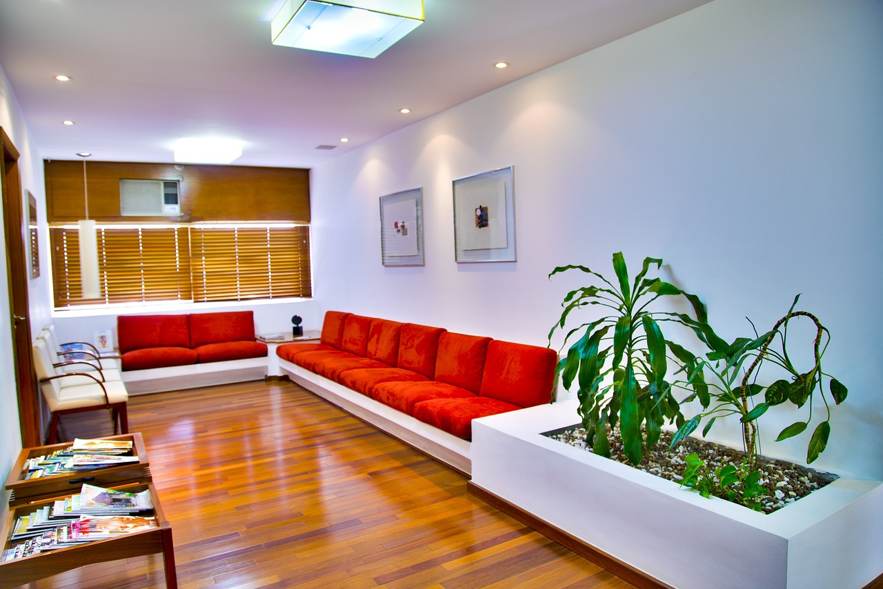 A waiting room or lounge, featuring orange plush couches and wood decor with white walls, with bamboo in a planter and tables of reading material