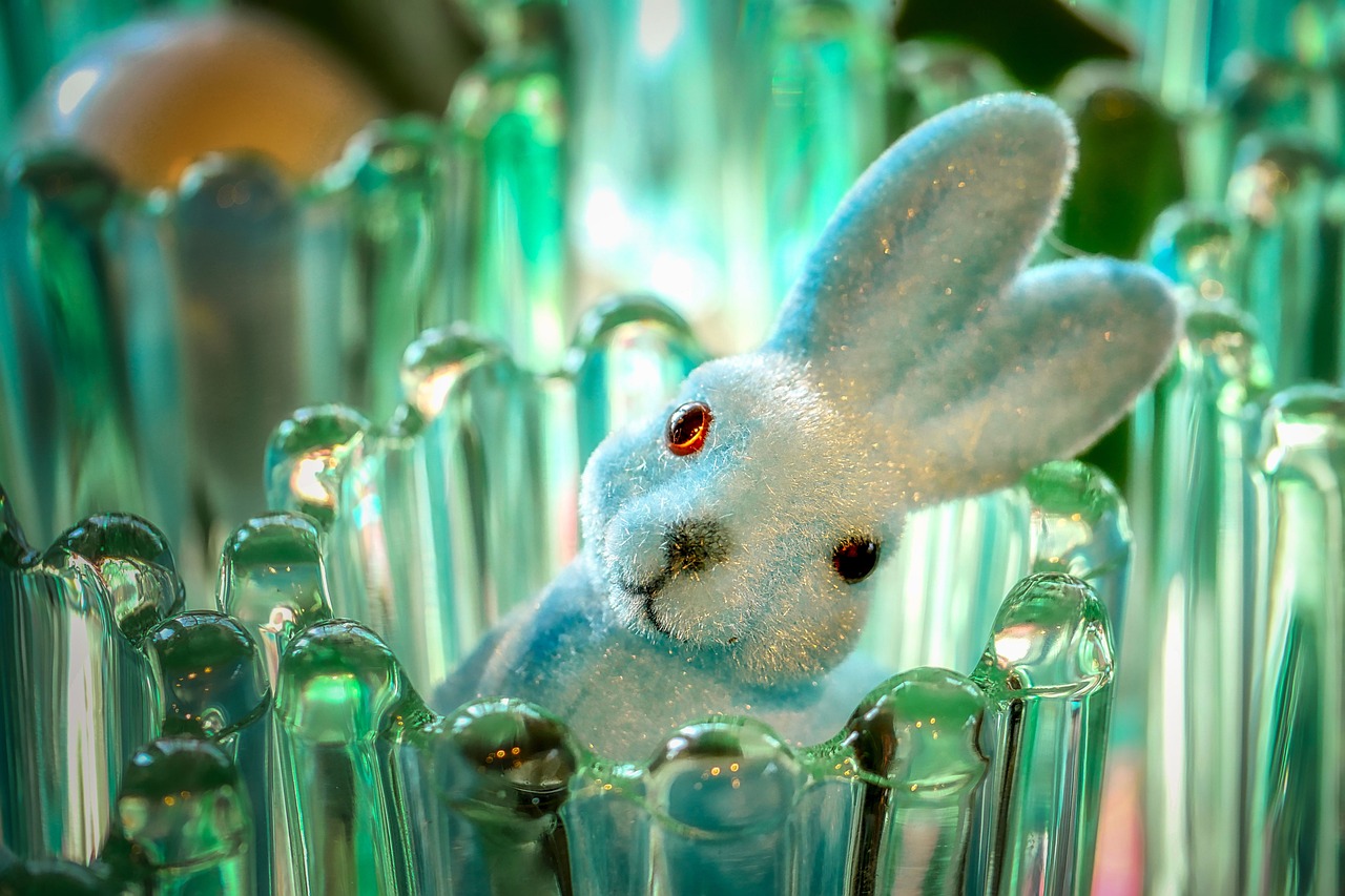 A glittery white bunny, cocking its head to the side, peeking out of one of many green glass candle holders