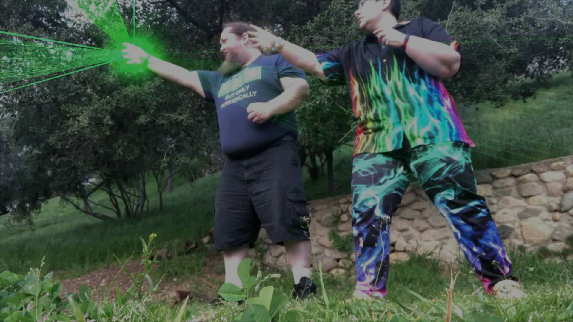 A heavyset man blasting electric green energy from his hand, while a heavyset person in rainbow flame clothing extends a globe of light from theirs against a green field